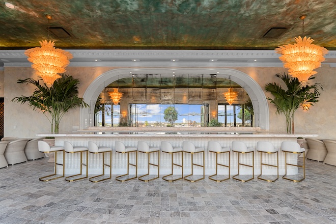 The inside of the bar with a copper ceiling, intricate chandeliers and white bar stools.