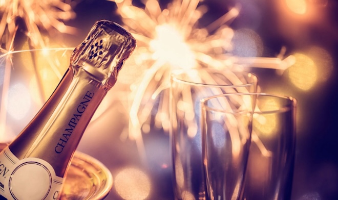 A champagne bottle and glasses in front of fireworks. 