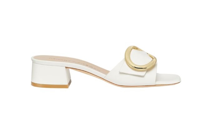 A casual white heel with an open-toe featuring a large gold detail across the front. 