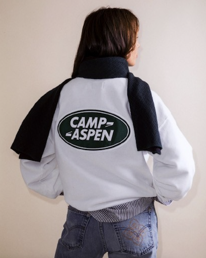 A model wearing a white jacket that has the "Camp Aspen" logo on the back.