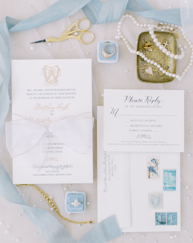 Blue, white, and gold flatlay, including invitations, jewelry, and pearls. 