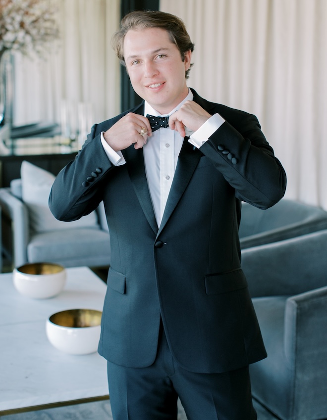 The groom adjusting his polka dot bow tie. 