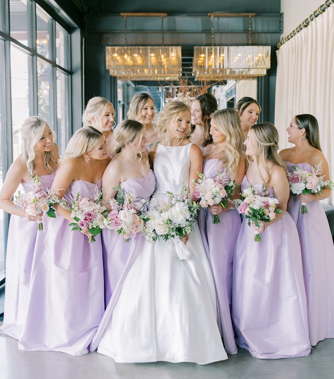 The bride posing with her bridesmaids wearing strapless purple dresses. 