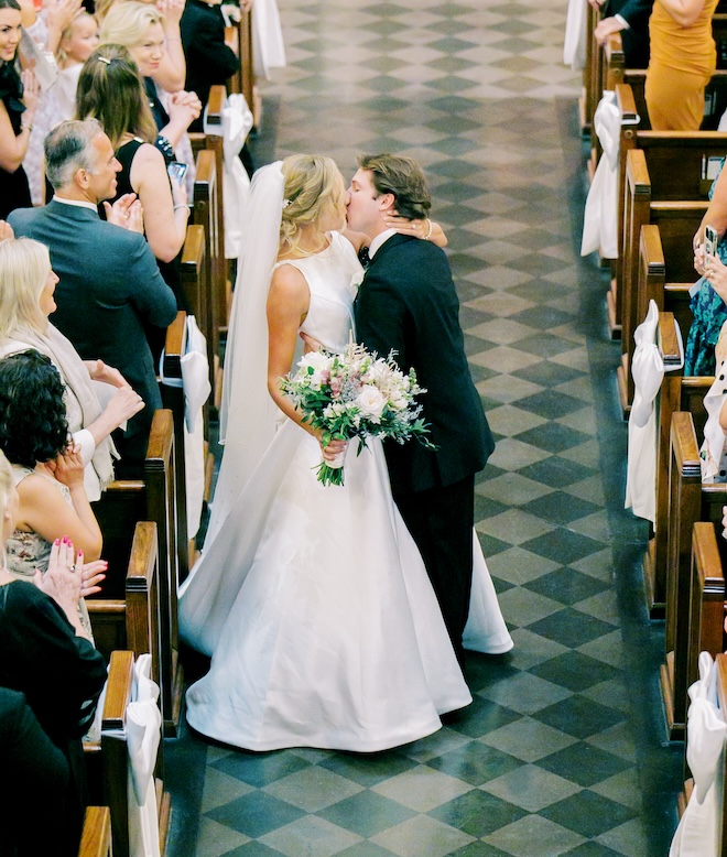 the bride and groom kissing in the middle of the aisle of the church. 