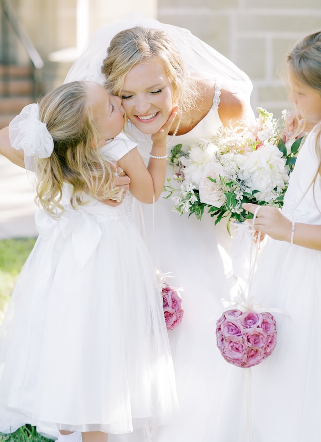 A flower girl kissing the bride on the cheek. 