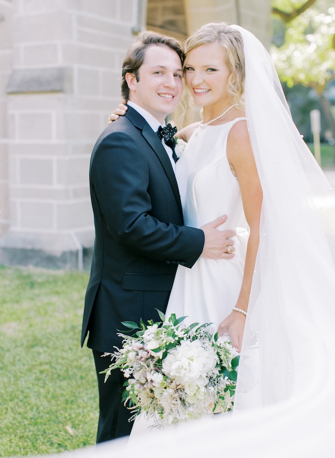 Bride and groom hugging and smiling outside of a church.