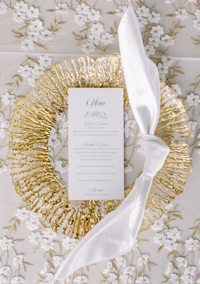 A gold plate with a black-and-white menu on a floral embroidered linen. 