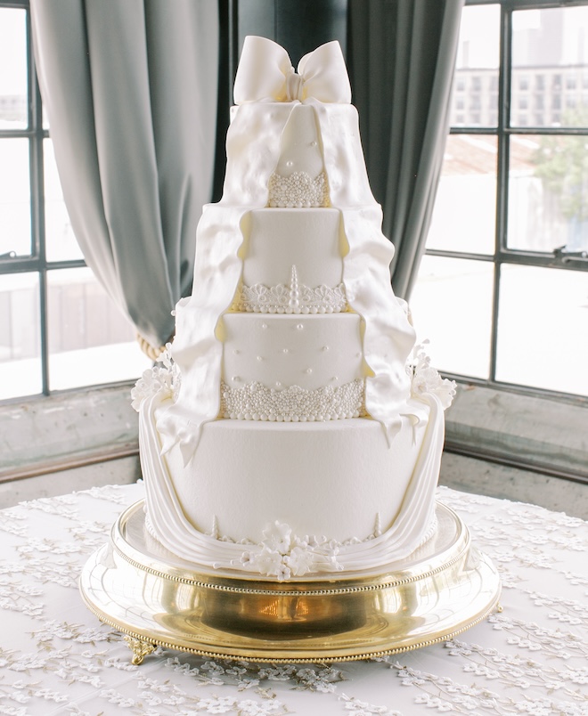 A four-tier white wedding cake with a bow at the top.