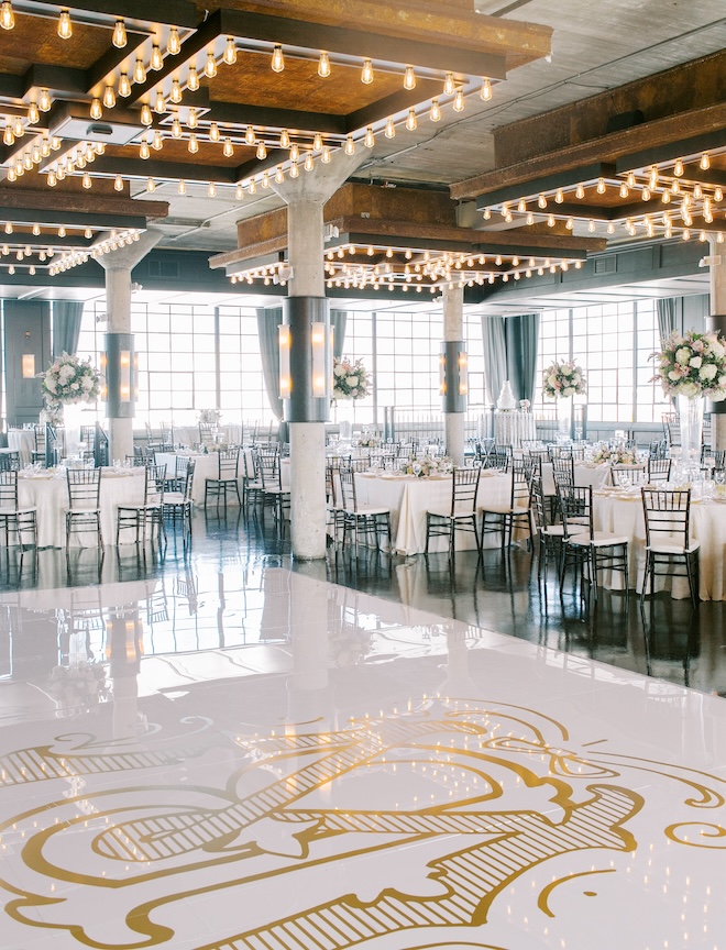 A white and gold monogrammed dance floor with reception tables surrounding it. 