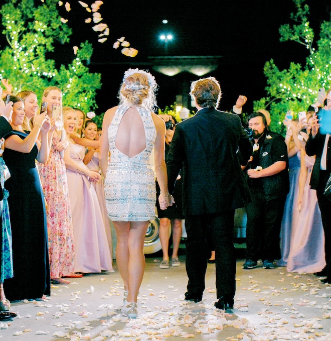 The bride wearing a mini dress and custom sneakers holding hands with her groom during their send off. 