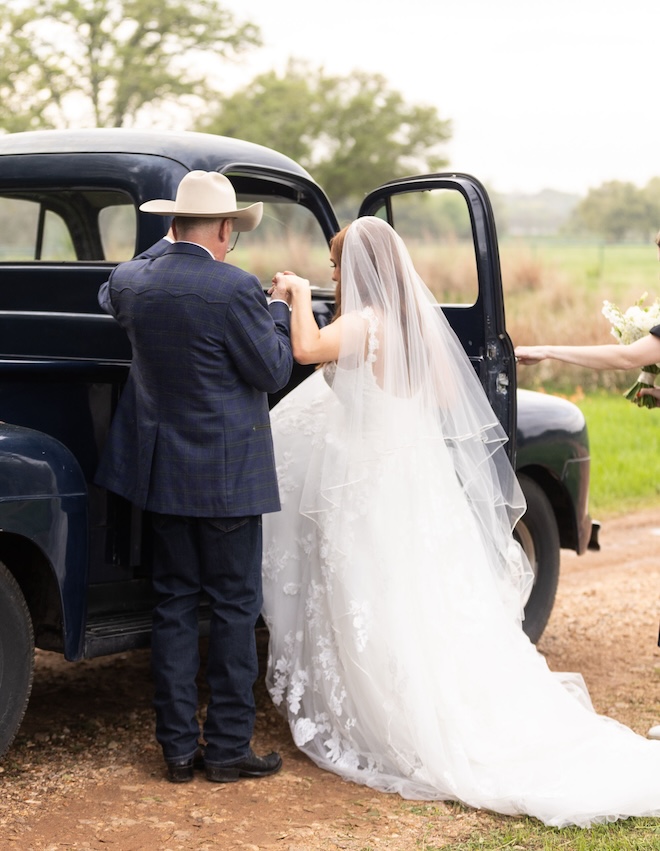 The bride's father helping the bride get into a vintage car. 