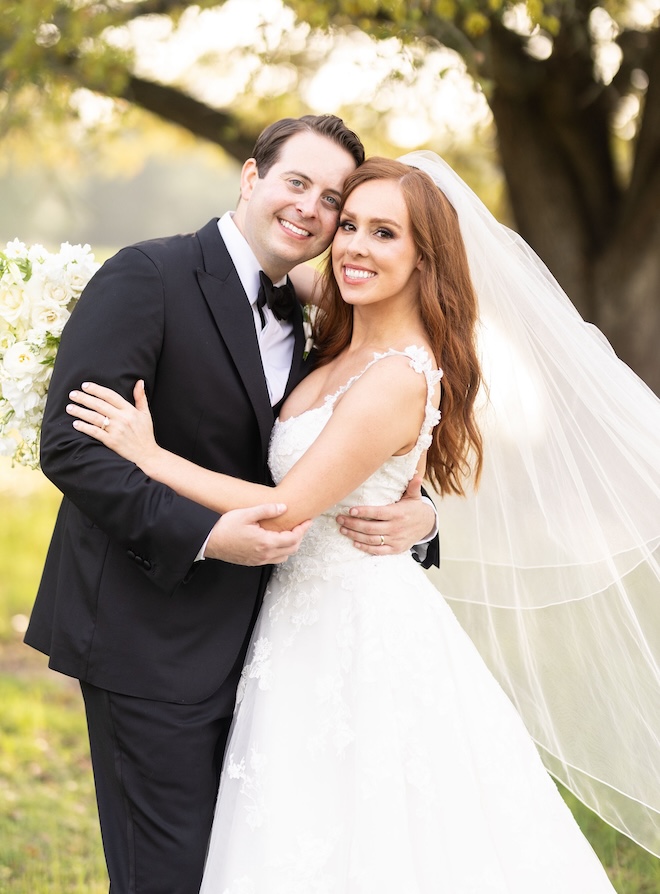 A bride and groom smiling in front of a large tree.