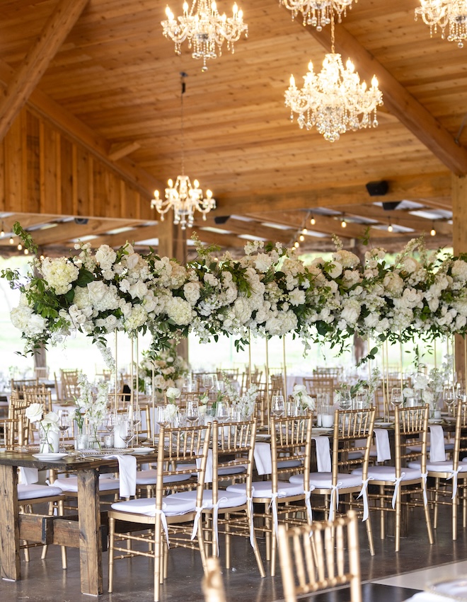 The reception in a barn venue with white floral centerpieces and gold chairs. 