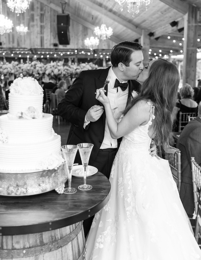 The bride and groom kissing white cutting into a 3-tier white wedding cake. 