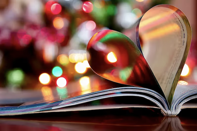 Pages of a book folded into a heart with Christmas lights in the background. 