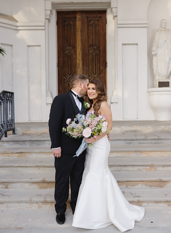 The groom kisses the bride on the cheek while standing outside the church in Galveston, Texas.