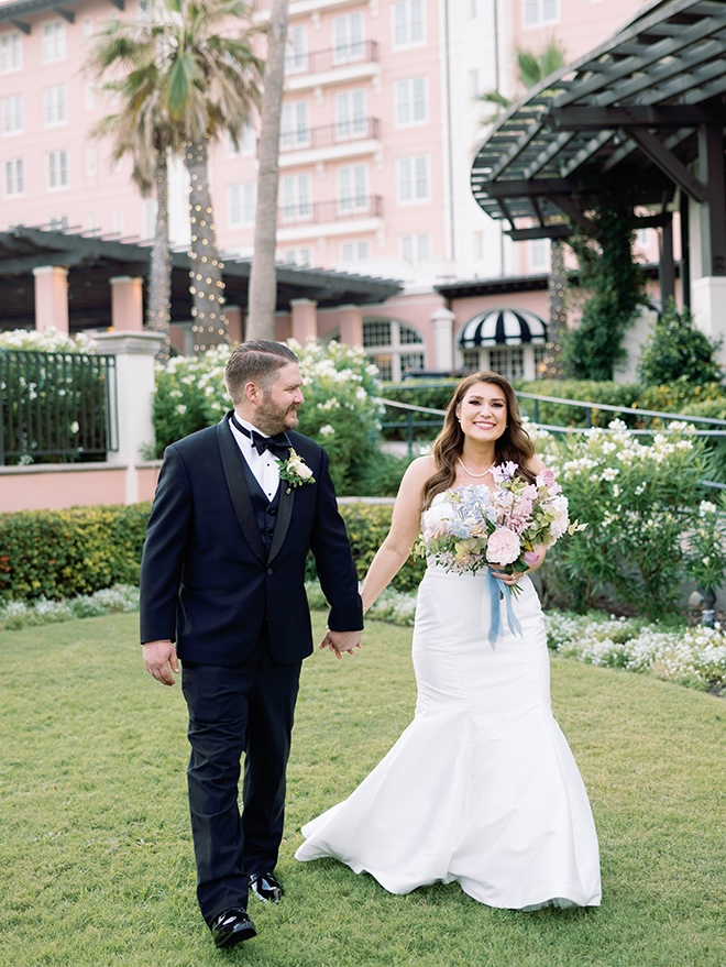 The bride and groom hold hands as they walk outside their wedding venue, the Grand Galvez.