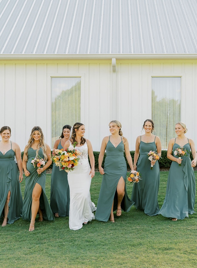 The bride and her bridesmaids walk outside their farmhouse wedding venue. 