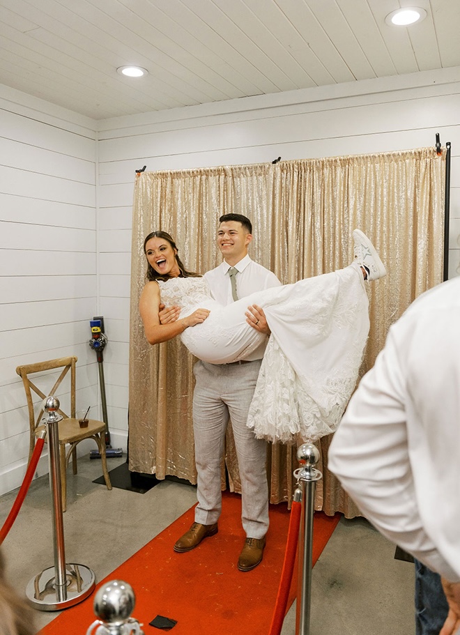 The groom picks up the bride for a picture in the photo booth. 