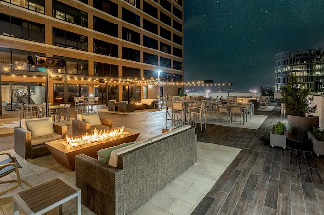 Lounge chairs and couches surrounded by a fire on the rooftop. 