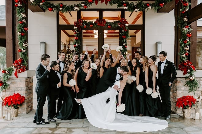 The bride and groom kissing while the wedding party cheers behind them. 