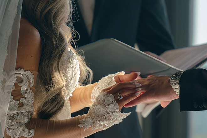 The bride puts the groom's wedding ring on his finger at their wedding ceremony.