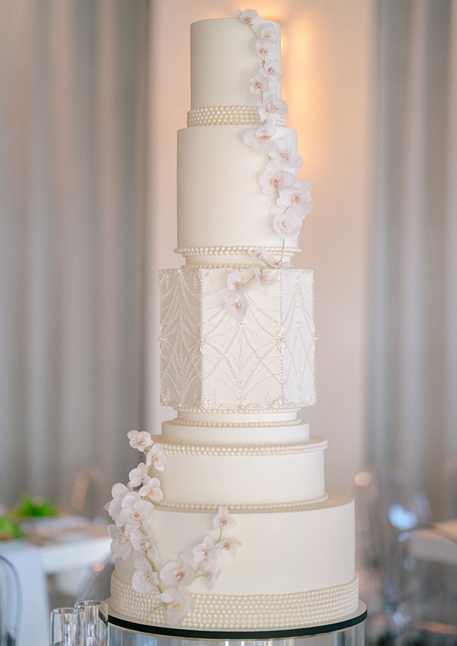 A white wedding cake is decorated in pearl detailing and orchids.