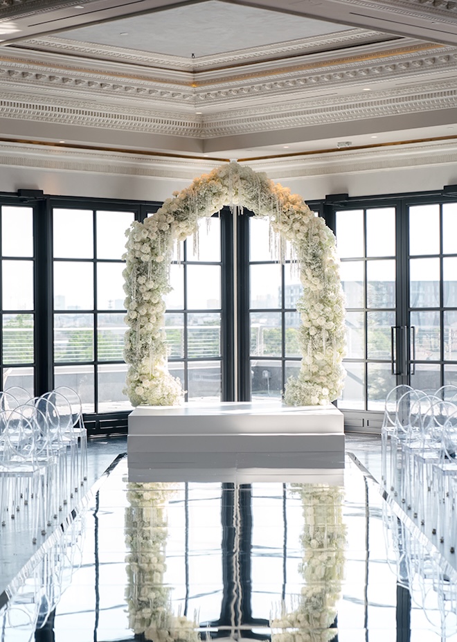 A floral arch detailed in roses and white baby's breath is the centerpiece for the couple's wedding ceremony at Le Tesserae. 