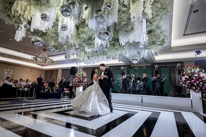 A bride and groom dancing on a black and white dance floor with a floral canopy and discos above them. 