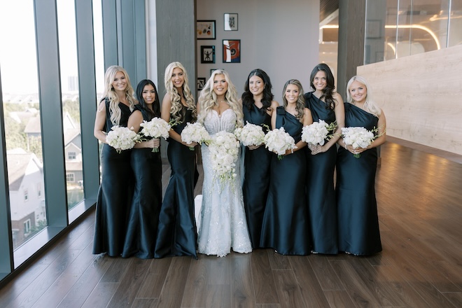 The bride standing with her bridesmaids in black one-shouldered gowns and white bouquets. 