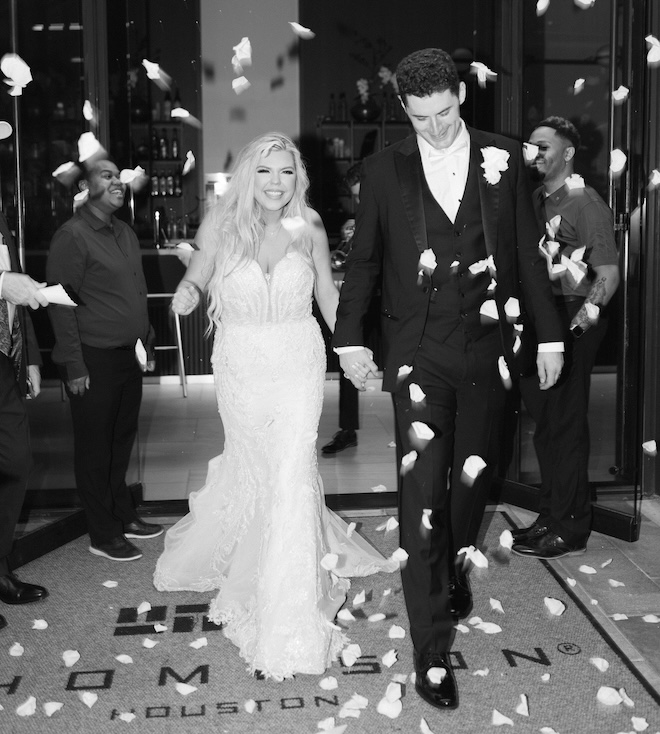 The bride and groom holding hands walking out of the Thompson Houston  with white rose petals being thrown. 