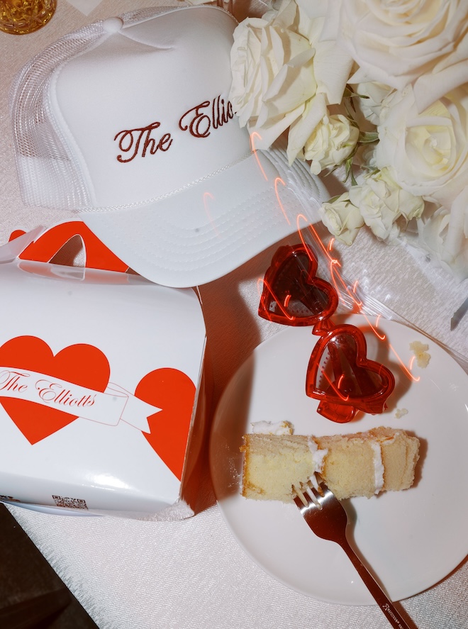 A white hat monogrammed with "The Elliotts", red heart sunglasses, a piece of cake, and a happy meal labeled "The Elliots"