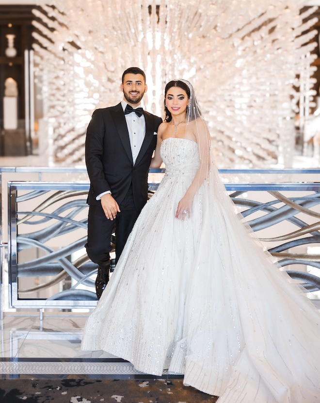 The bride and groom smiling in front of the large chandelier at The Post Oak Hotel at Uptown Houston. 