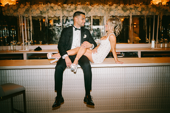 The couple sit on top of the bar at their wedding reception at Le Tesserae. 