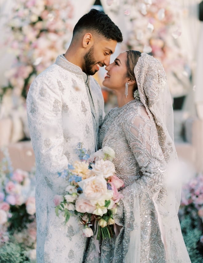 The bride and groom looking at each other wearing traditional Muslim outfits surrounded by pastel florals. 