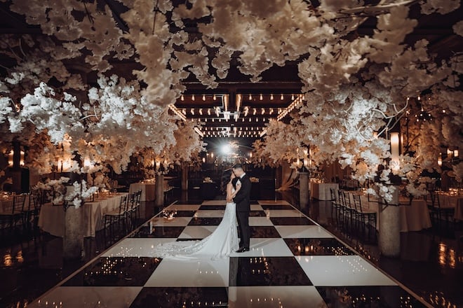 A bride and groom dancing on a black and white checkered dance floor with white florals surrounding them. 