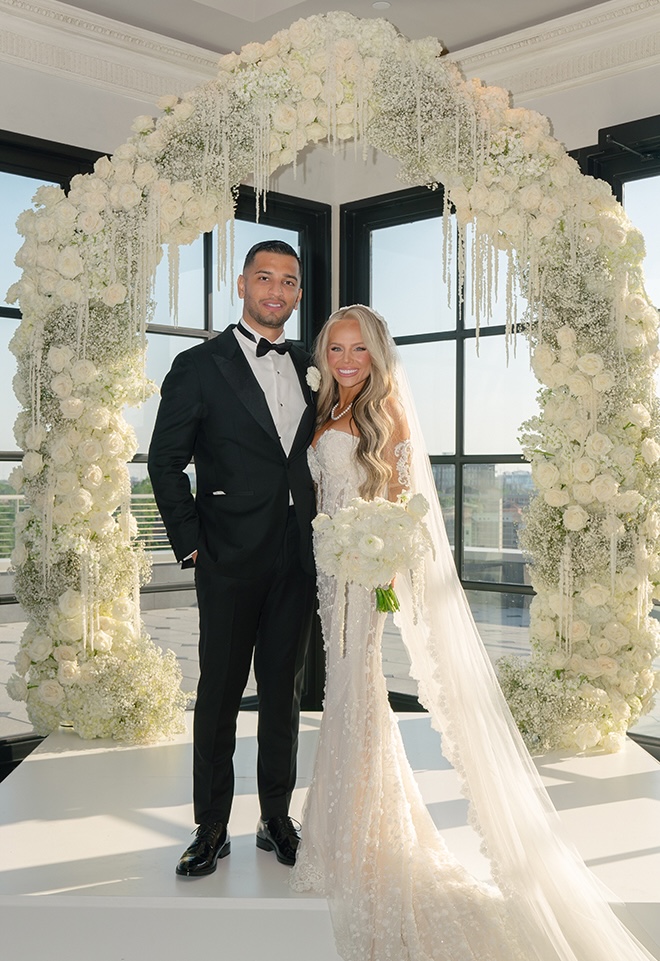 The bride and groom smile under their wedding floral arch as the Houston skyline serves as the backdrop. 