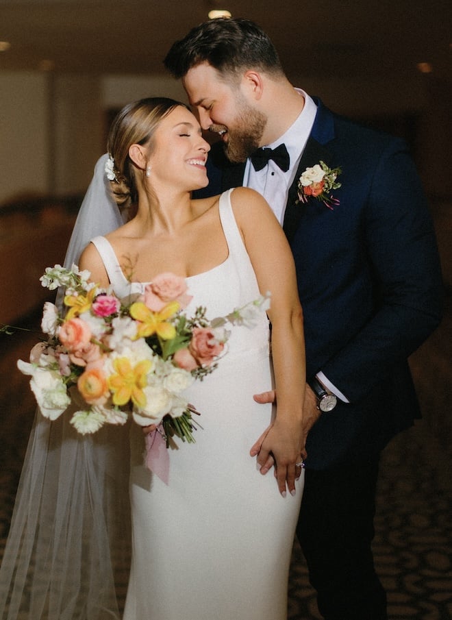 The bride and groom smiling at each other with the bride holding a colorful bouquet. 