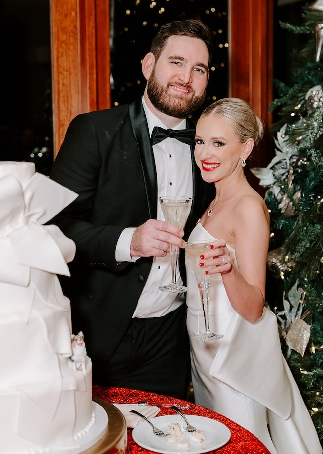 The bride and groom holding up champagne flutes next to their wedding cake. 