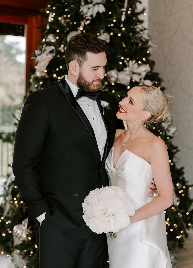 Bride and groom looking at each other while standing in front of a Christmas tree. 