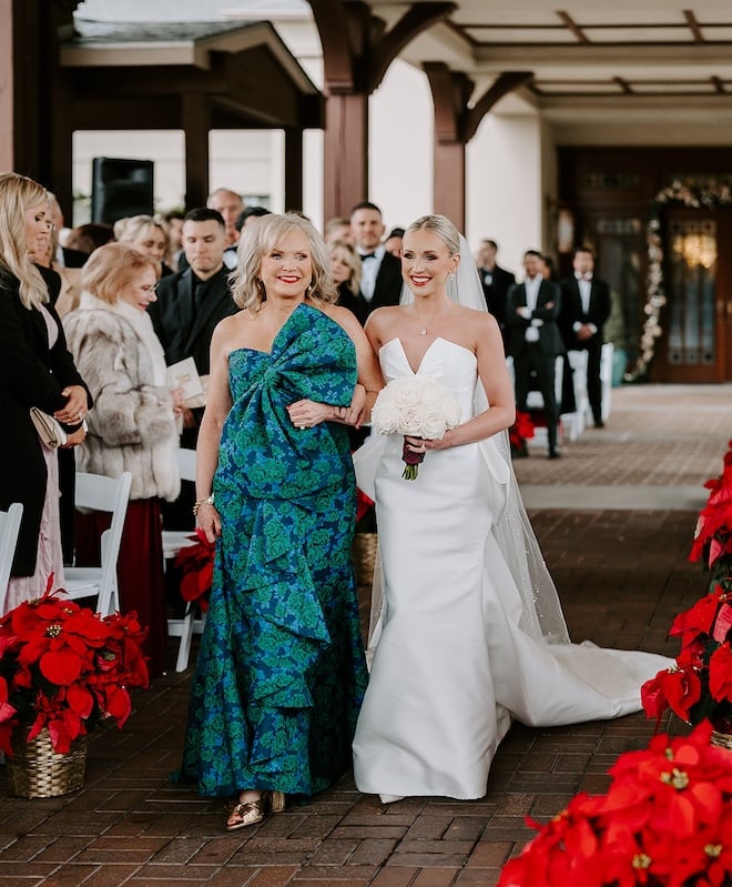 The bride and her mother walking down the poinsettia-lined aisle. 