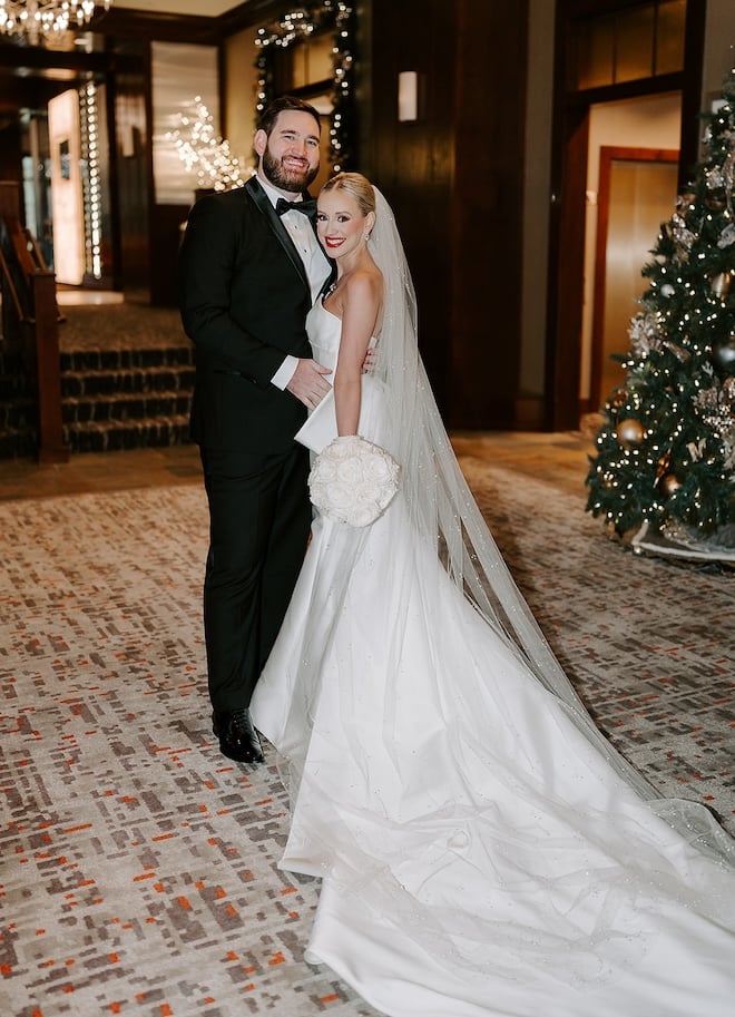 The bride and groom smiling with a Christmas tree behind them. 