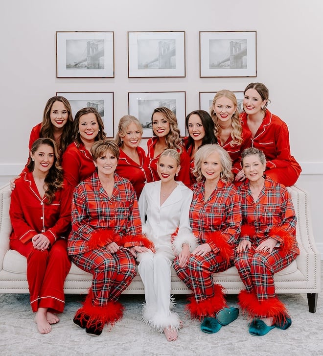 The bride in a white pajama set while her bridesmaids and the mother's of the couples wear plaid and red pajamas. 