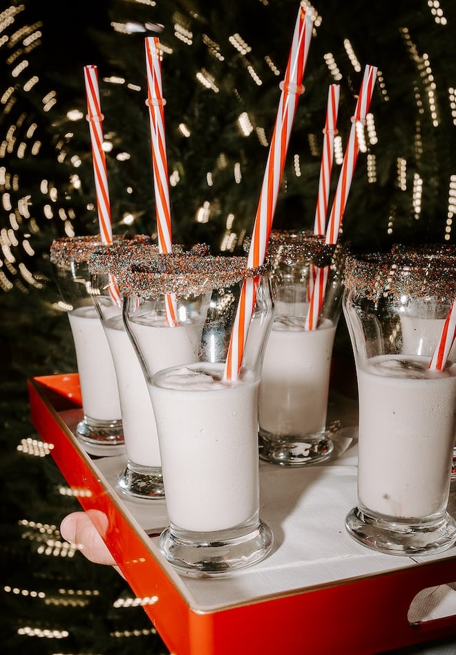 A tray of egg nog with sprinkles on the rim of the glass with red and white striped straws. 