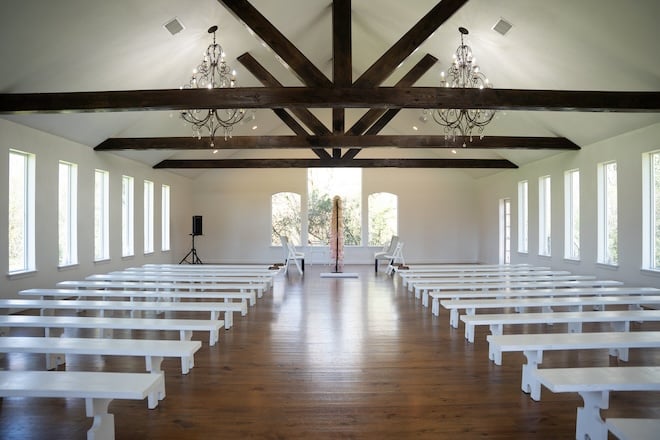 The chapel at Venue 311, a white chapel with wooden beams, chandeliers and white pews. 