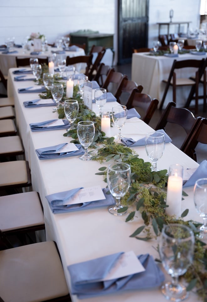 The reception tables with greenery in the center and white and blue linens. 