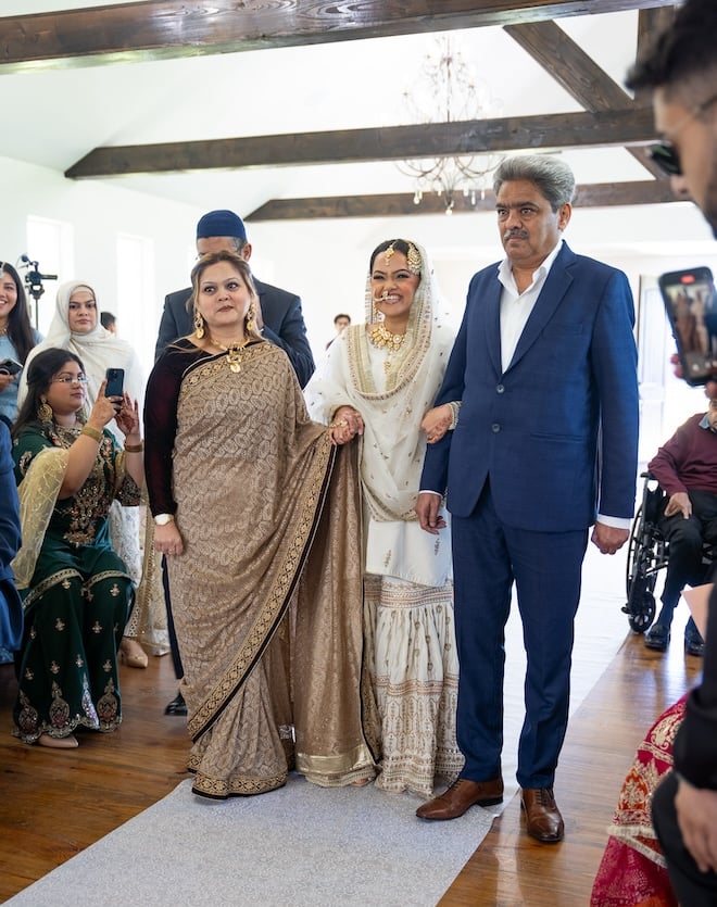 The bride smiling big while her parents walk her down the aisle. 