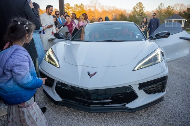 The bride and groom about to drive away from the reception in a white corvette. 