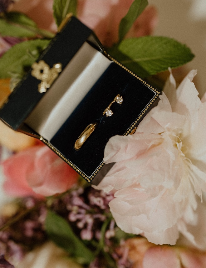 A ring box holding a gold and diamond ring surrounded by flowers. 