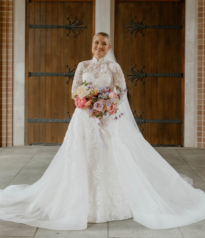 The bride wearing an all-lace gown with a bouquet of colorful florals. 